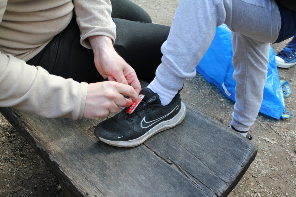 Nahaufnahme: Eine Hand befestigt eine Startnummer am Schuh eines Kindes.