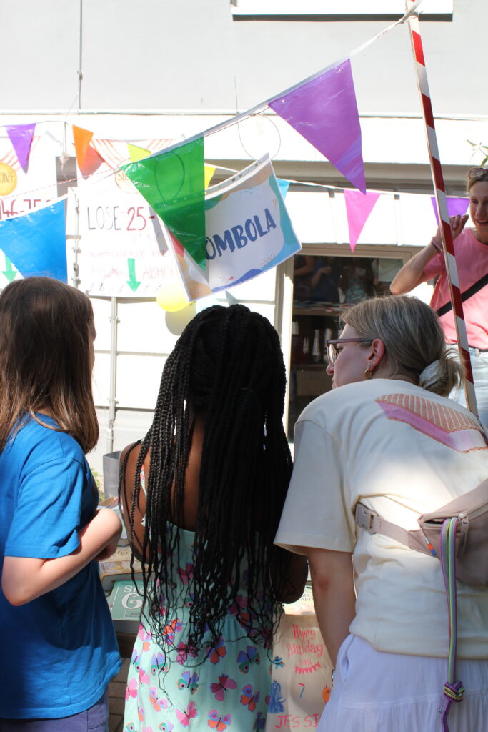 Kinder vor einem Stand mit Tombola-Schild und bunten Wimpeln.