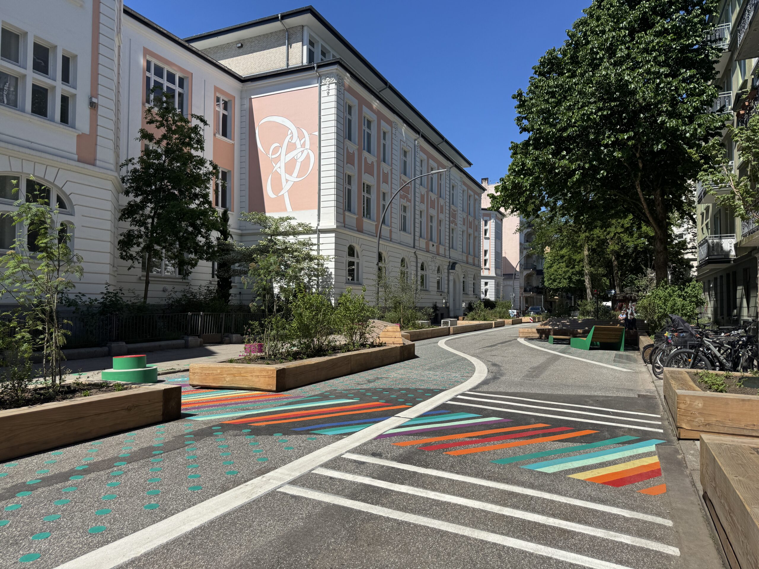 Das historische Schulgebäude der Schule Rellinger Straße mit dem geschwungenen Relli-Logo auf der rosa Fassade, davor die bunt gestaltete Spielstraße.