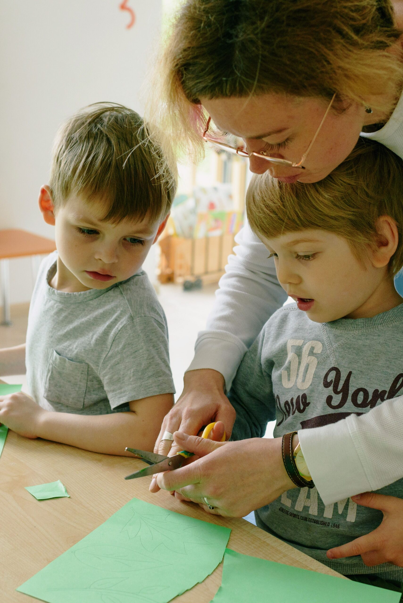 Eine Erwachsene schneidet mit zwei Kindern Papier aus.