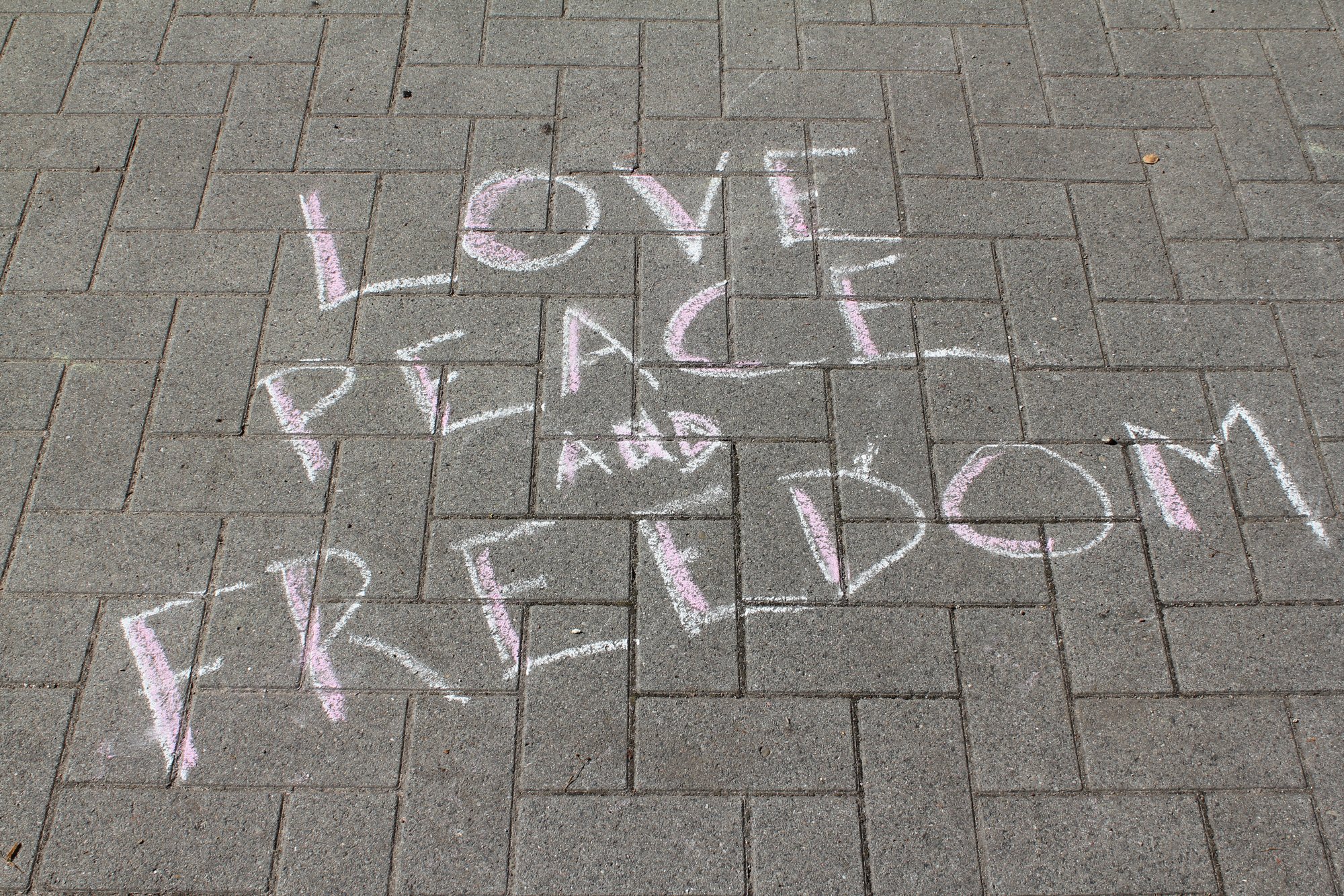Kreideschrift auf dem Pflaster: Love, Peace and Freedom.
