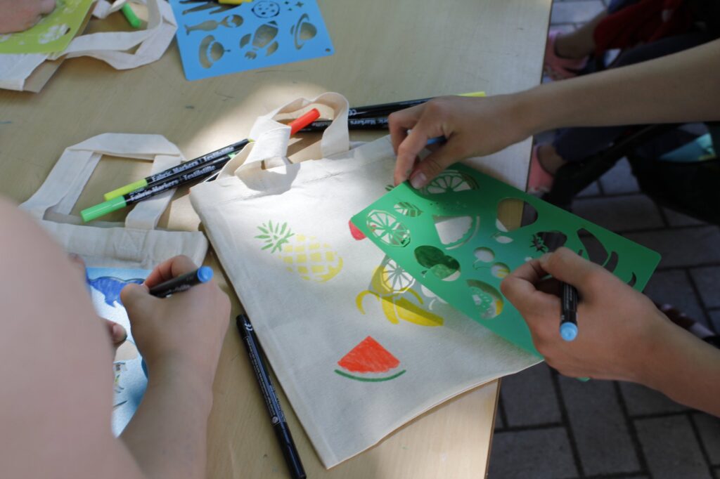 Kinder bemalen Stofftaschen mit Schablonen und Filzstiften.