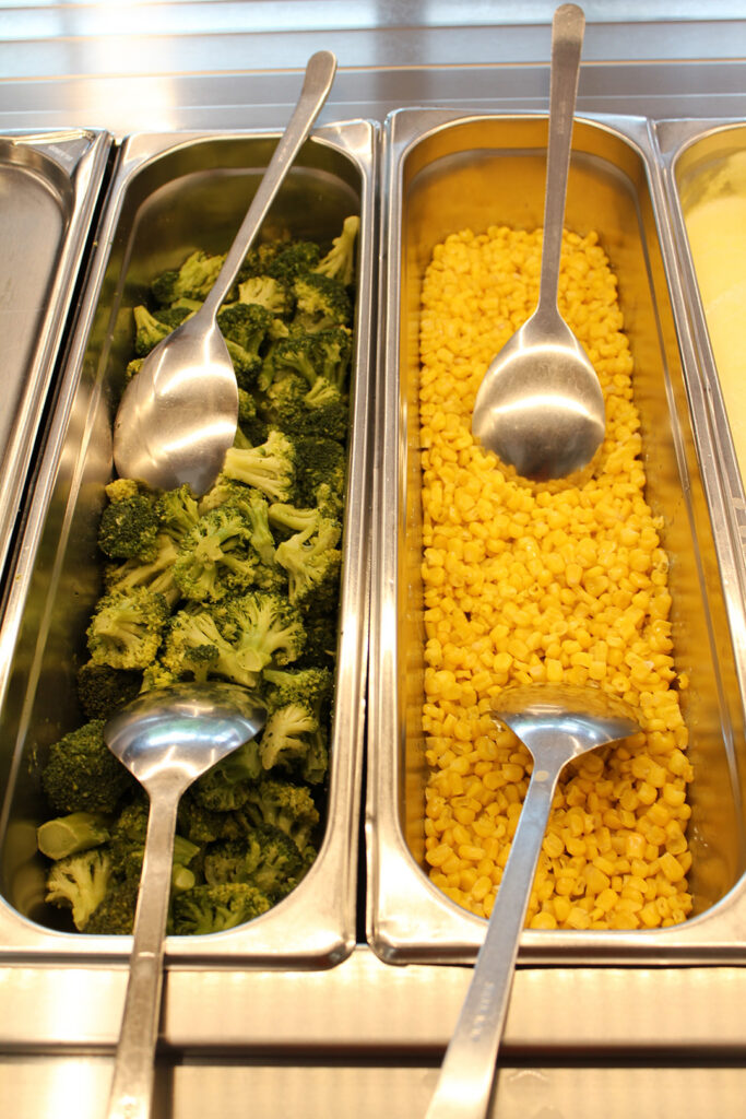 Warmes Mittagessen in Behältern am Buffet: Brokkoli und Mais.