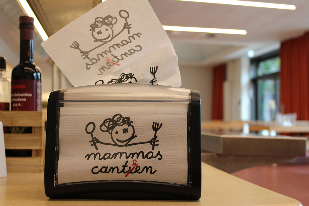 Serviettenspender mit dem Logo von mammas canteen auf einem Mensatisch.