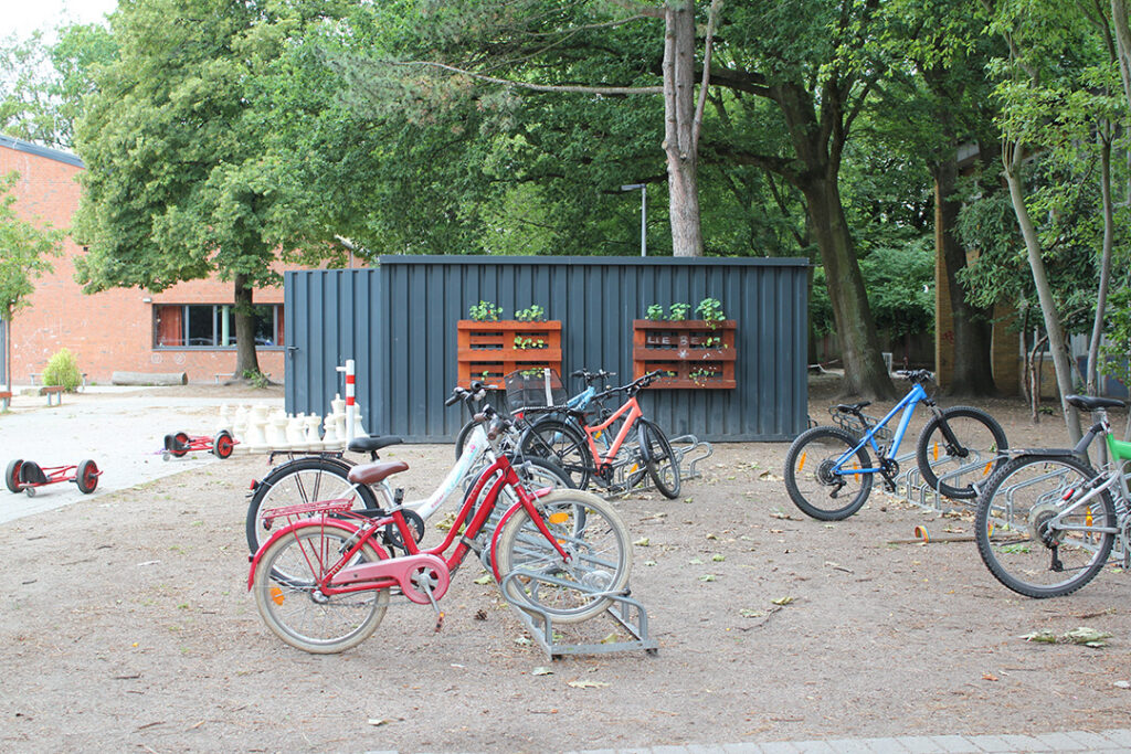 Fahrradständer mit Kinderfahrrädern auf dem Schulhof vor einem Container.