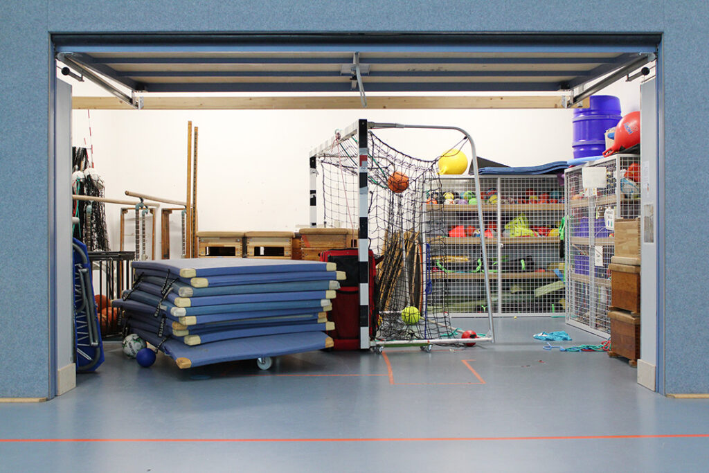 Geräteraum der Sporthalle mit Matten, Bällen und Netzen.