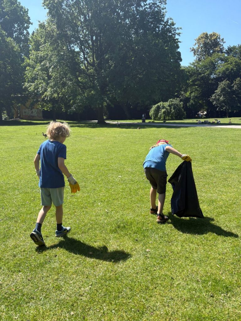 Zwei Kinder sammeln mit einem schwarzen Müllsack Müll im Park