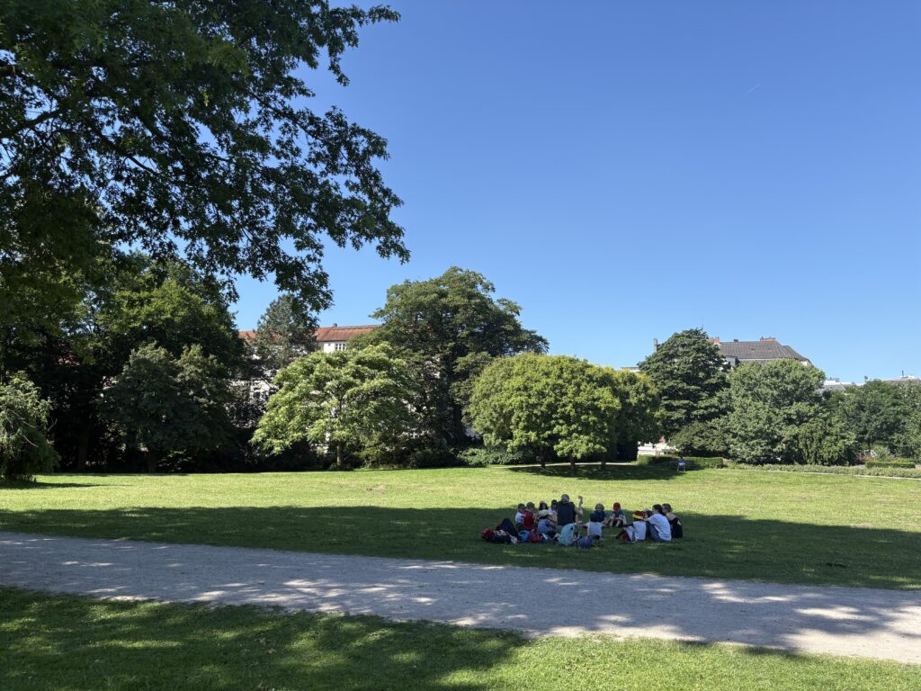 Die Kinder sitzen im Kreis auf einer großen Wiese im Hayns Park