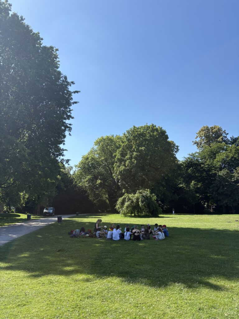 Die Lerngruppe sitzt im Kreis im Schatten der Bäume