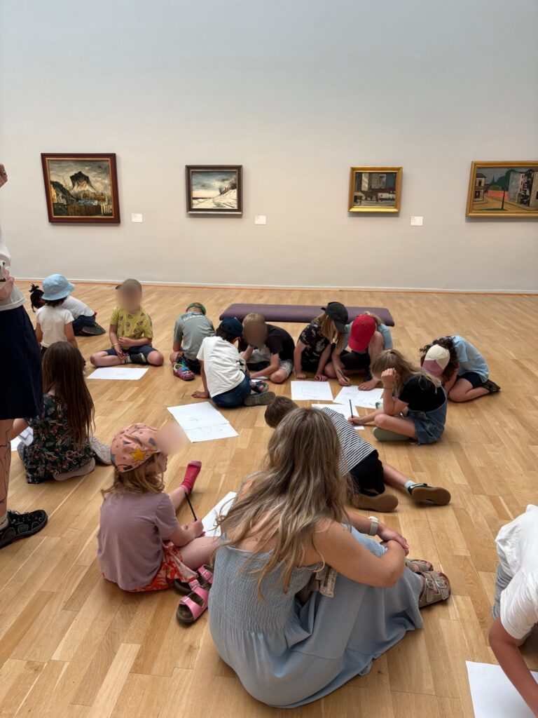 Kinder zeichnen im Ausstellungsraum, vorne sitzt eine Begleiterin