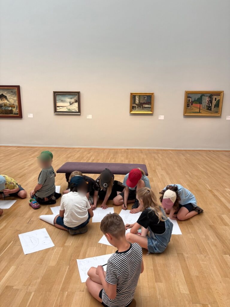 Kinder sitzen in der Kunsthalle auf dem Boden und zeichnen auf großen Papierbögen