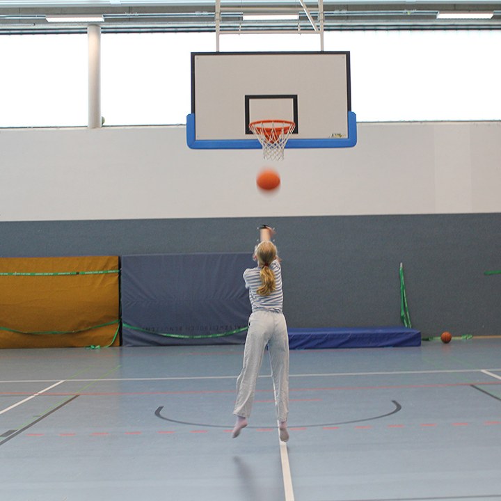 Ein Kind wirft in der Sporthalle einen Basketball auf den Korb.