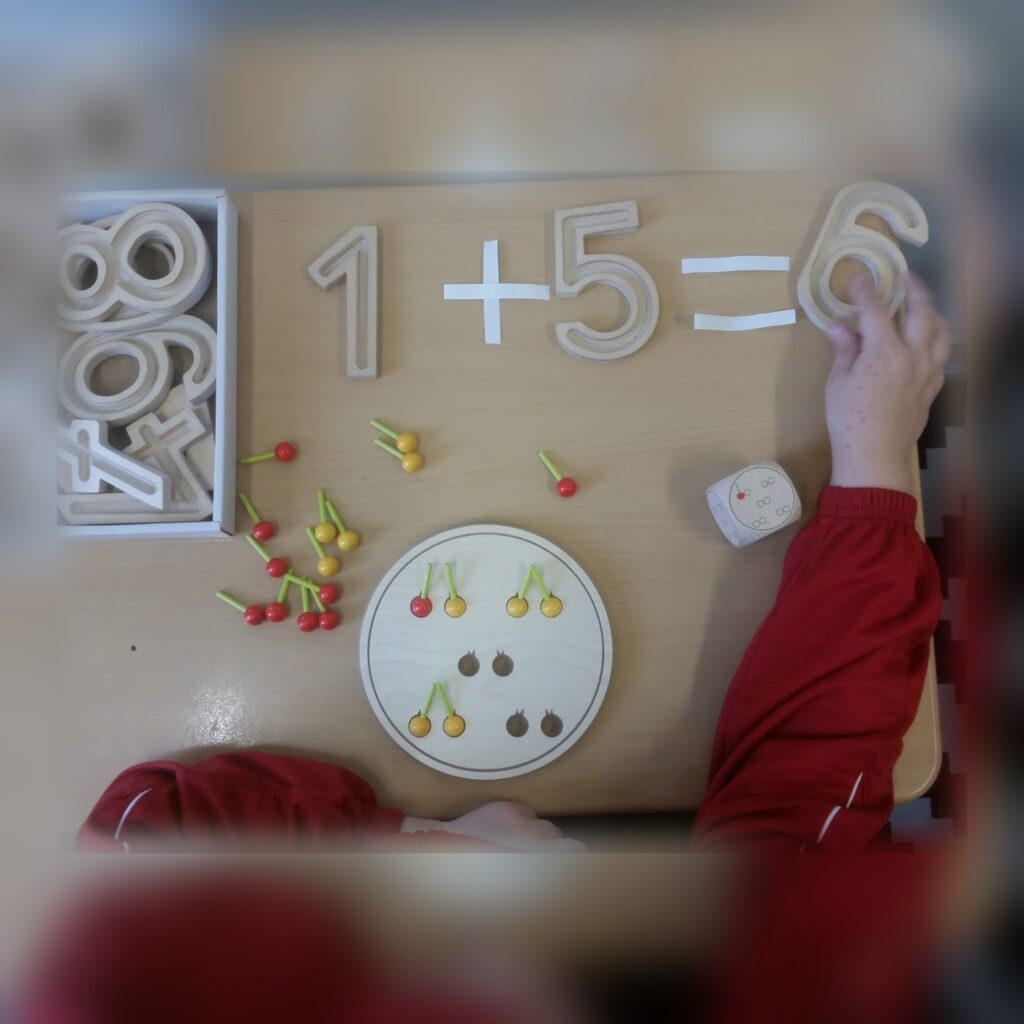 Rechenaufgabe 1 plus 5 gleich 6 aus Holzziffern, daneben Zählmaterial.