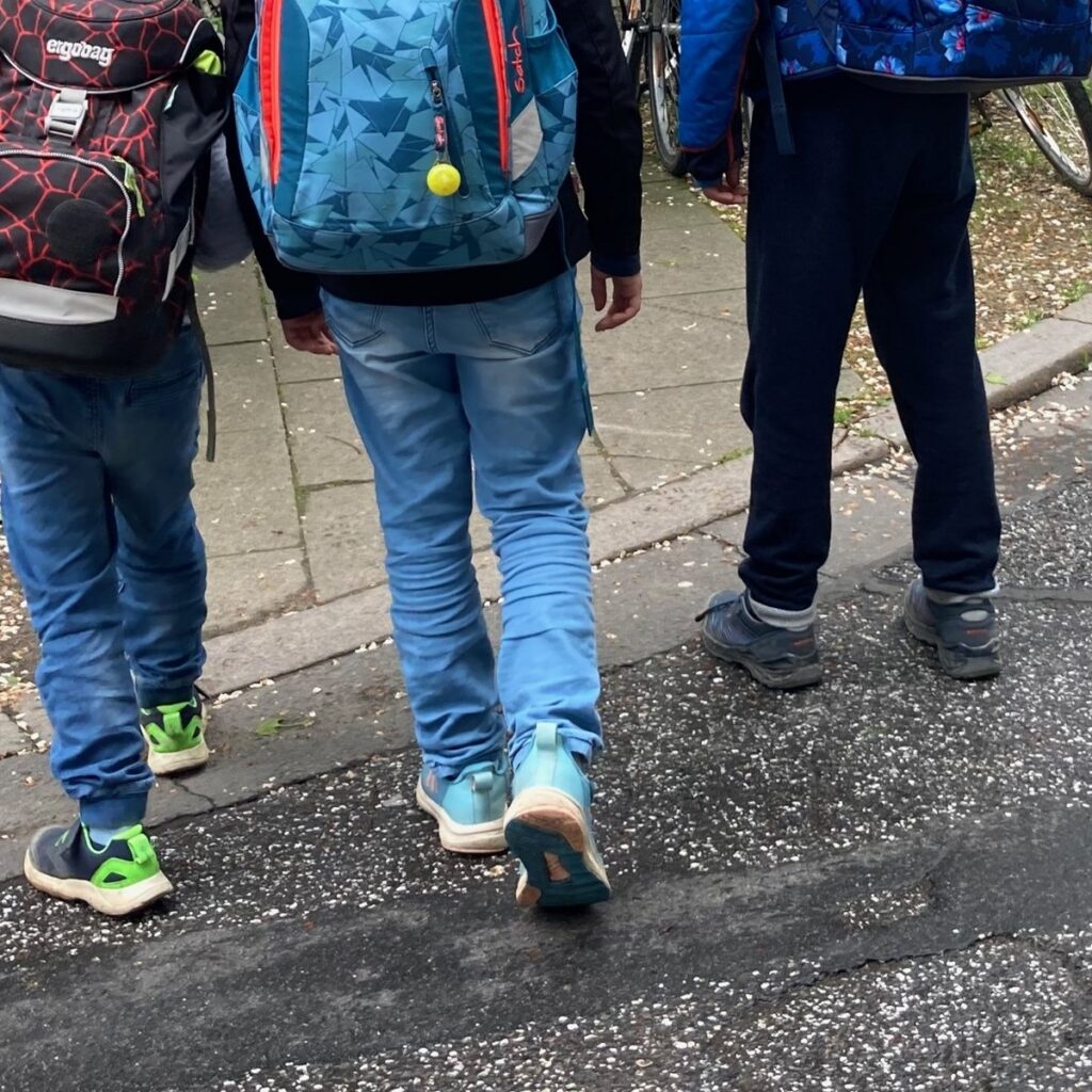 Drei Kinder mit Schulranzen auf dem Schulweg, von hinten fotografiert.