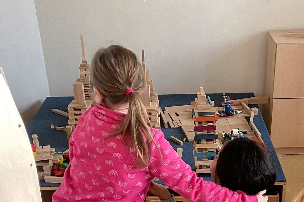 Zwei Kinder bauen mit Holzklötzen eine große Stadt.