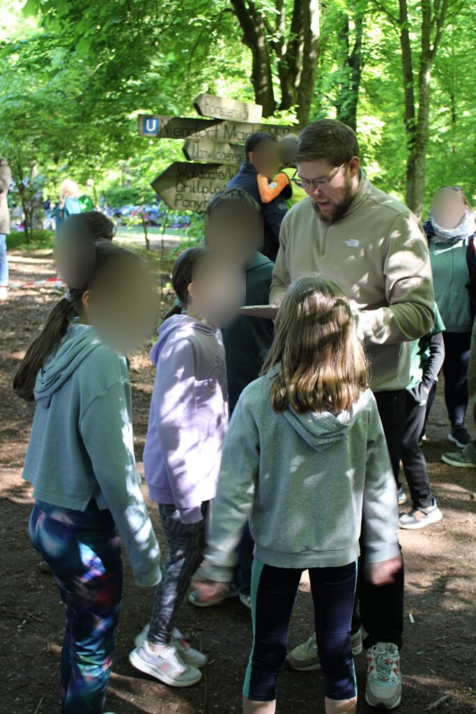 Ein Lehrer und mehrere Kinder stehen im Wald zusammen.