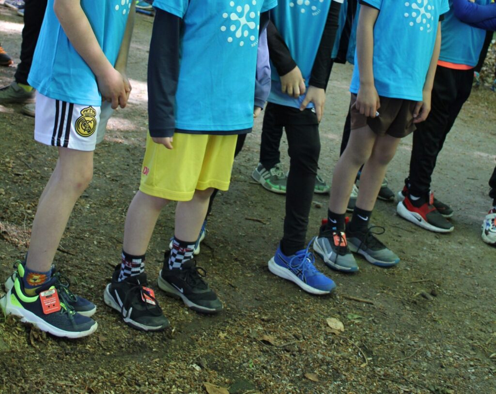 Beine von Kindern in Relli-T-Shirts und Sportschuhen beim Waldlauf.